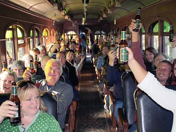 Large group of passengers celebrating aboard a 1880 Train vintage passenger car, raising bottles of beer and cheering