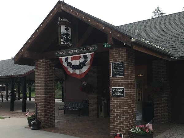 1880 Train Hill City depot brick ticket office building with Train Tickets and Gifts sign and patriotic bunting, Hill City, South Dakota