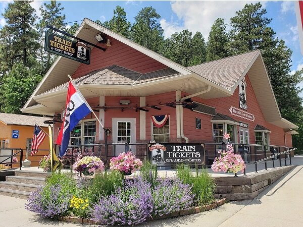 1880 Train Keystone depot building decorated with flowers and patriotic flags, surrounded by pine trees, Keystone, South Dakota