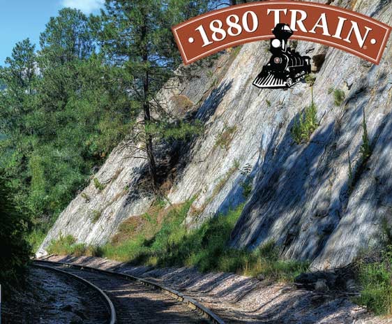 train tracks through the rocks and trees with the 1880 Train logo